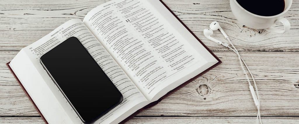 Holy Bible and smartphone with black coffee cup on wooden background.